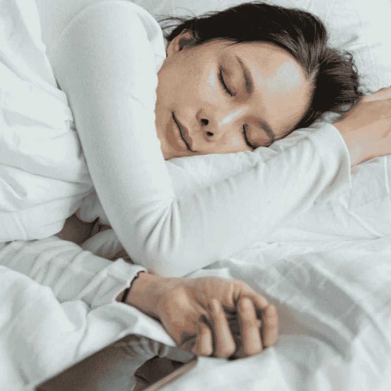 Una mujer está durmiendo en la cama con un teléfono móvil
